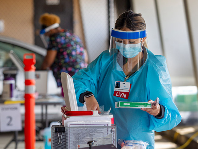 medical worker wearing protective gear and taking vaccine out of container
