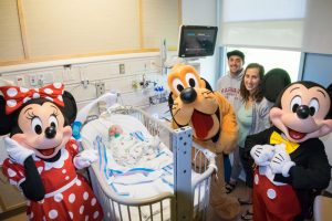 Mickey and Minnie Mouse and Pluto surround a child in a hospital bed.