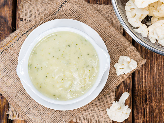 Creamy cauliflower soup in a bowl with two cauliflower florets on the table to the side.