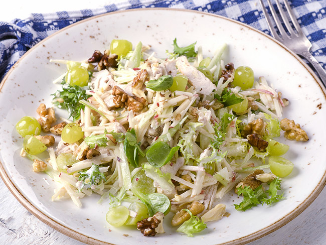 Chicken Waldorf salad served in a white ceramic bowl on a blue and white checkered tablecloth. 