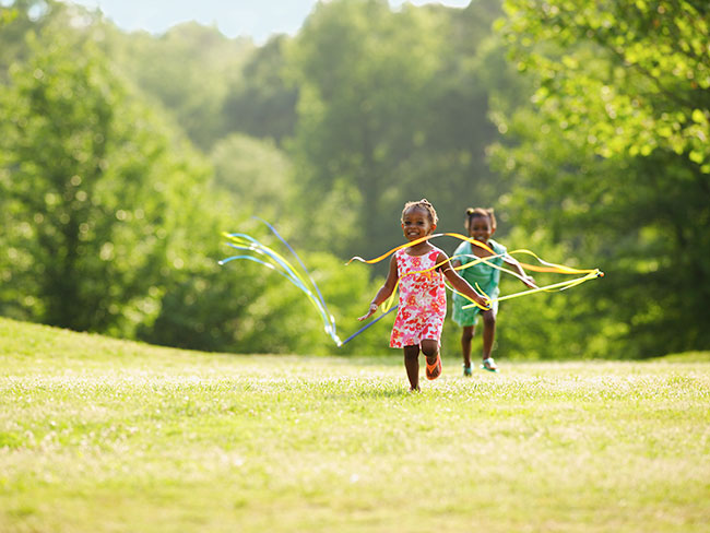 2 young girls running in a field with ribbons