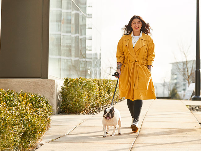 A woman is walking her dog and wearing a yellow jacket.
