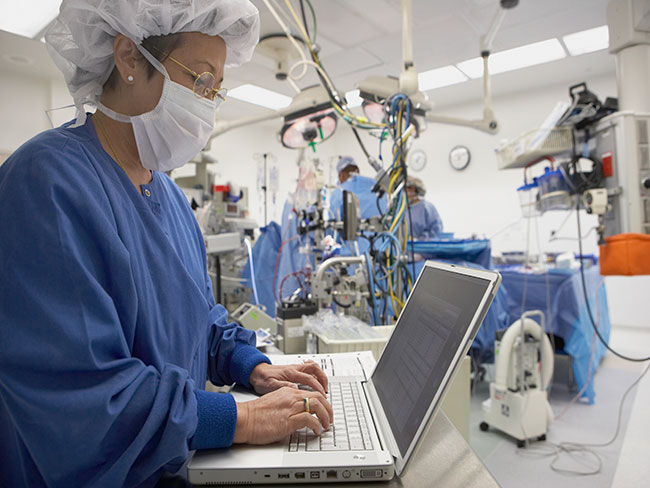 Nurse standing at laptop in operating room.