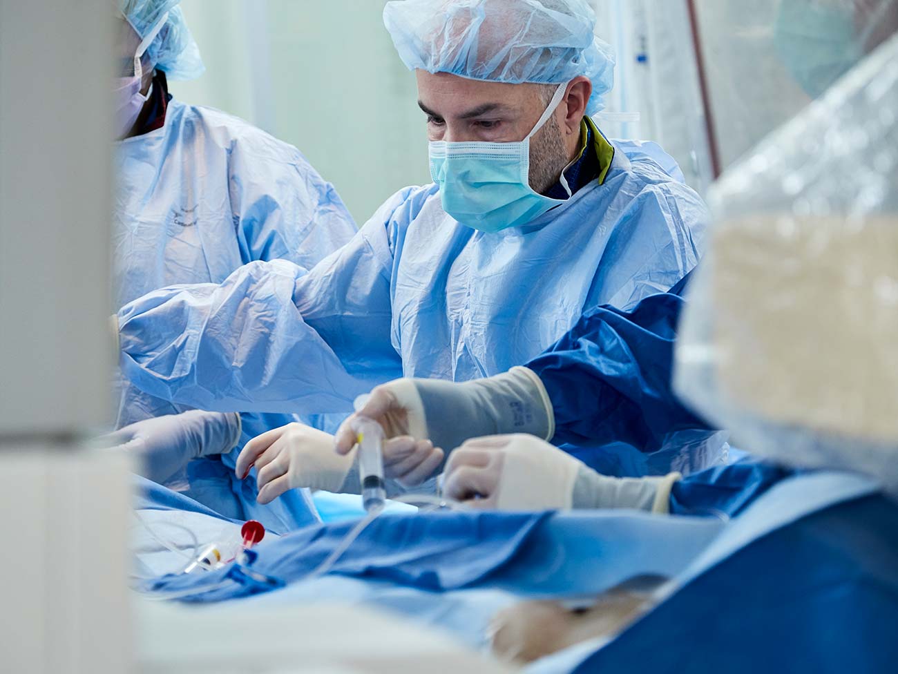 man wearing scrubs and a surgical mask performing surgery on a patient 