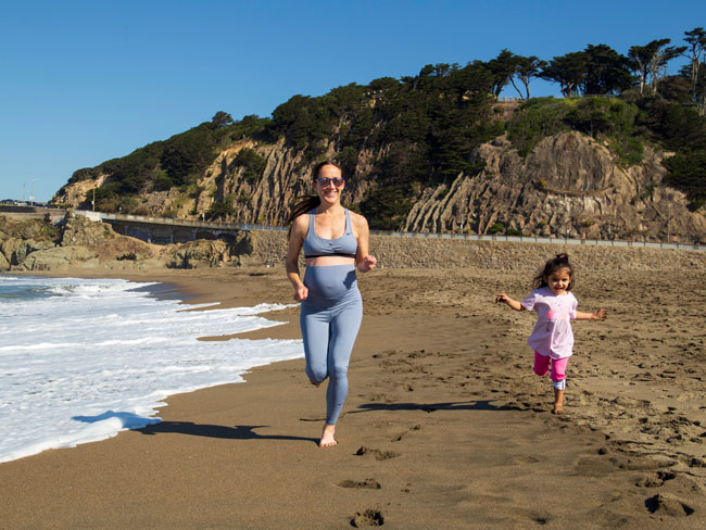 pregnant woman with young girl jogging on beach