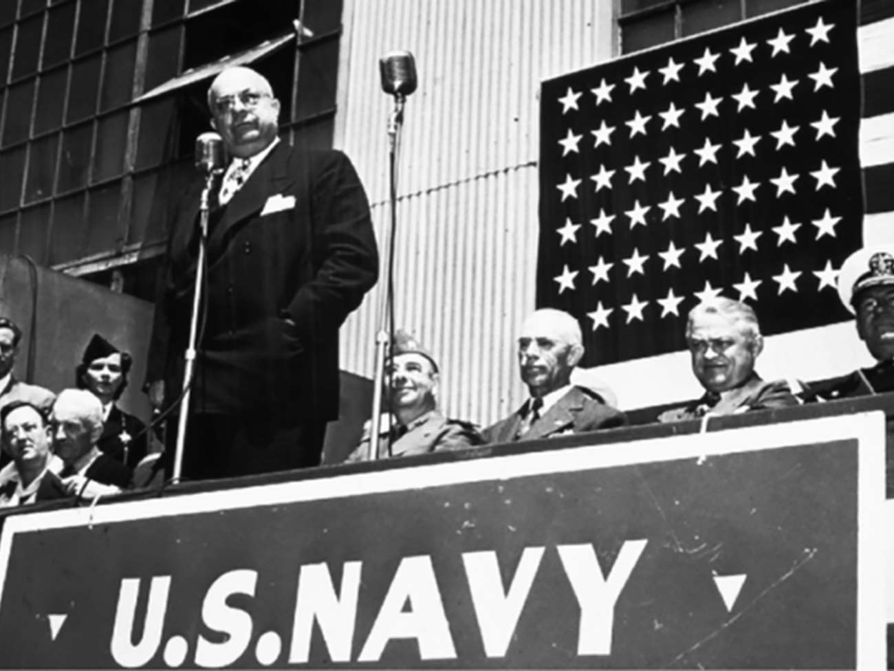 Henry J. Kaiser at a podium with a sign that reads: U.S. Navy