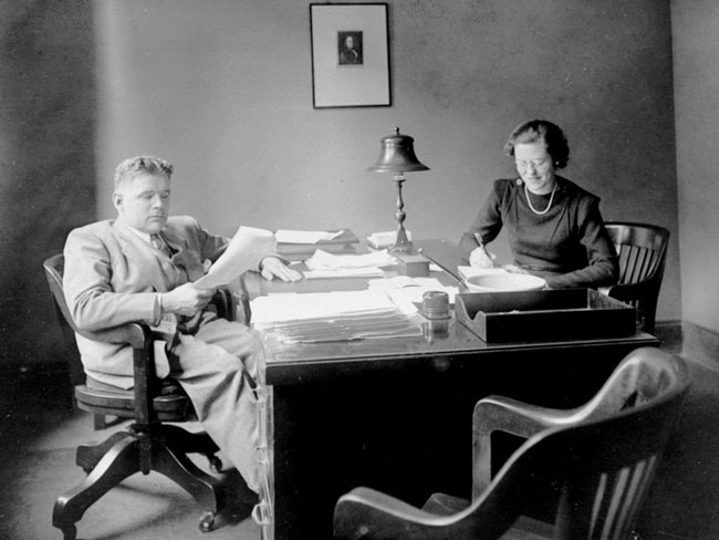 Harold Hatch and secretary Bess Girgitch reading the newspaper at a desk