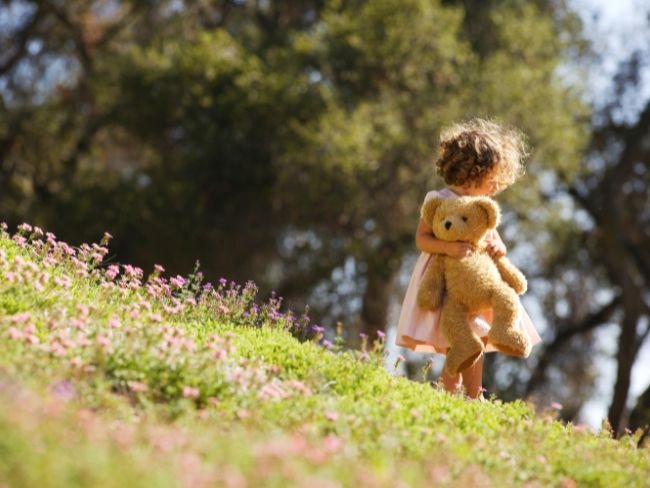 young girl in field holding teddy bear