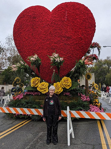 Lynn stands in the front of the gian red heart on the KP Rose Parade float