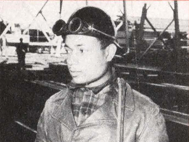 Black and white photograph of a man in the Kaiser Richmond shipyard wearing a hard hat and goggles on his head