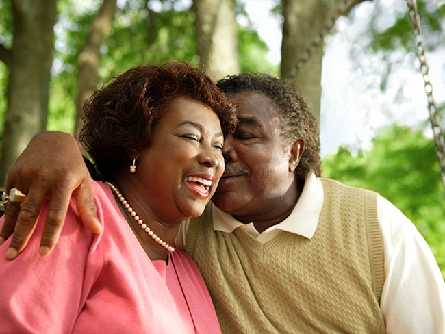 older man and woman in an outdoor setting smiling and cuddling