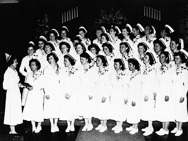 1951 graduating class of the Permanente Foundation Nursing School standing and facing Dorothea Daniels standing at the left