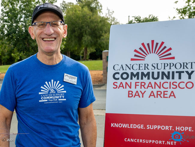 smiling man standing next to sign for Cancer Support Community San Francisco Bay Area