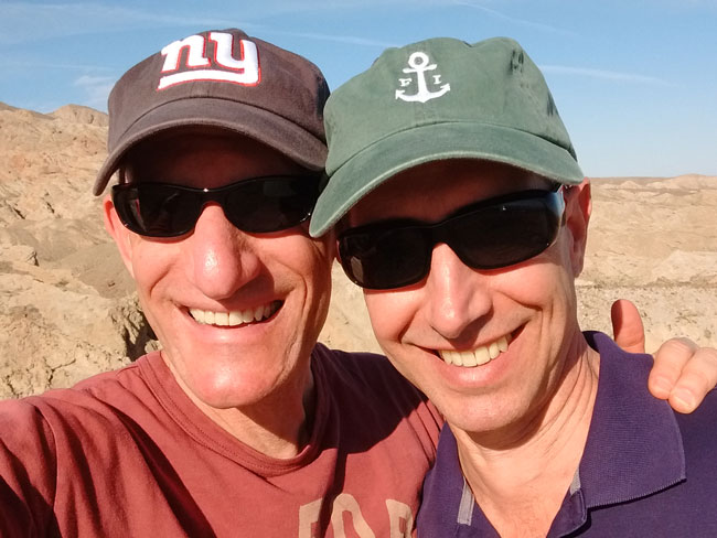 2 smiling men outdoors wearing sunglasses and caps