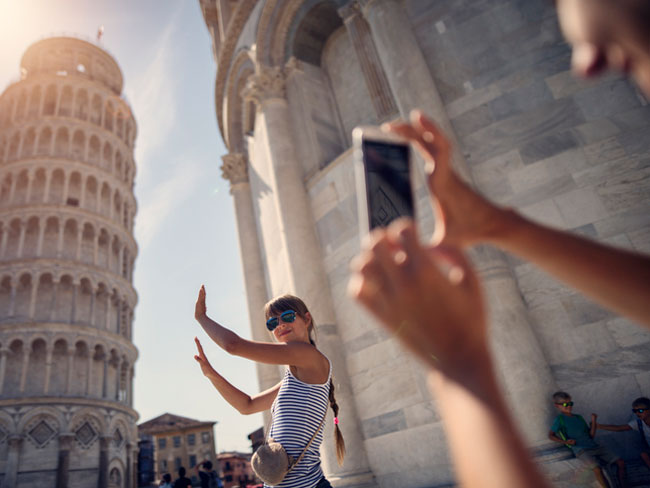 Teen taking picture with the Leaning Tower of Pisa in the background