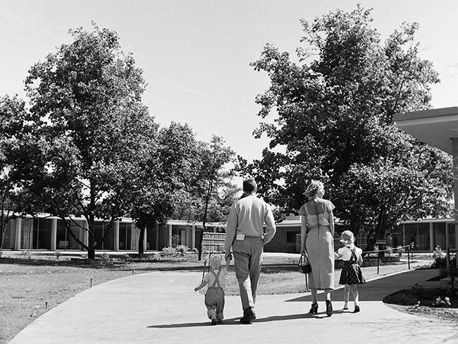 family walking along concrete path toward building surrounded by grass and trees