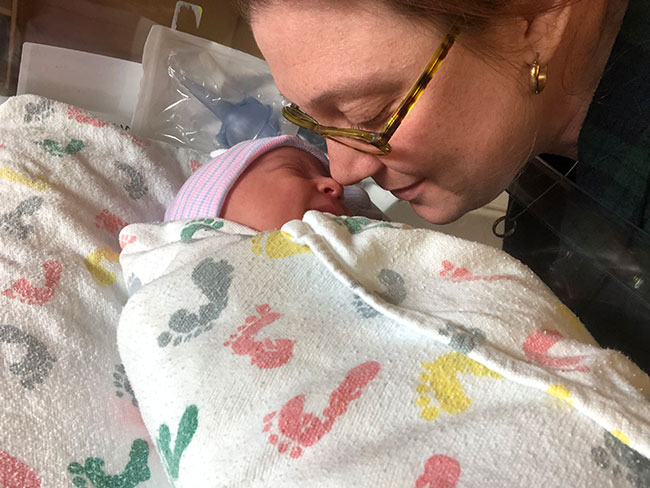 Alexia Rostow leans over newborn and their noses touch.
