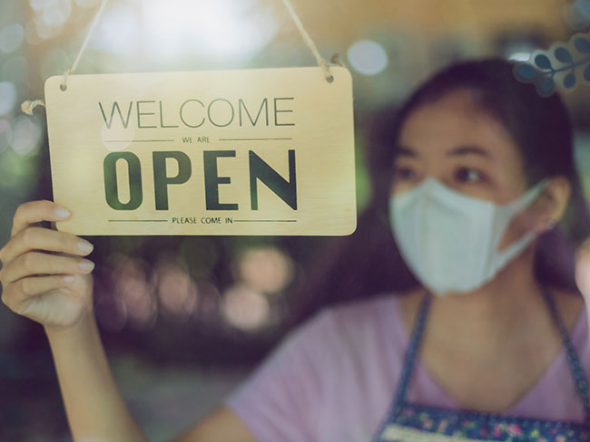 Asian woman with a mask on hold a business is open sign