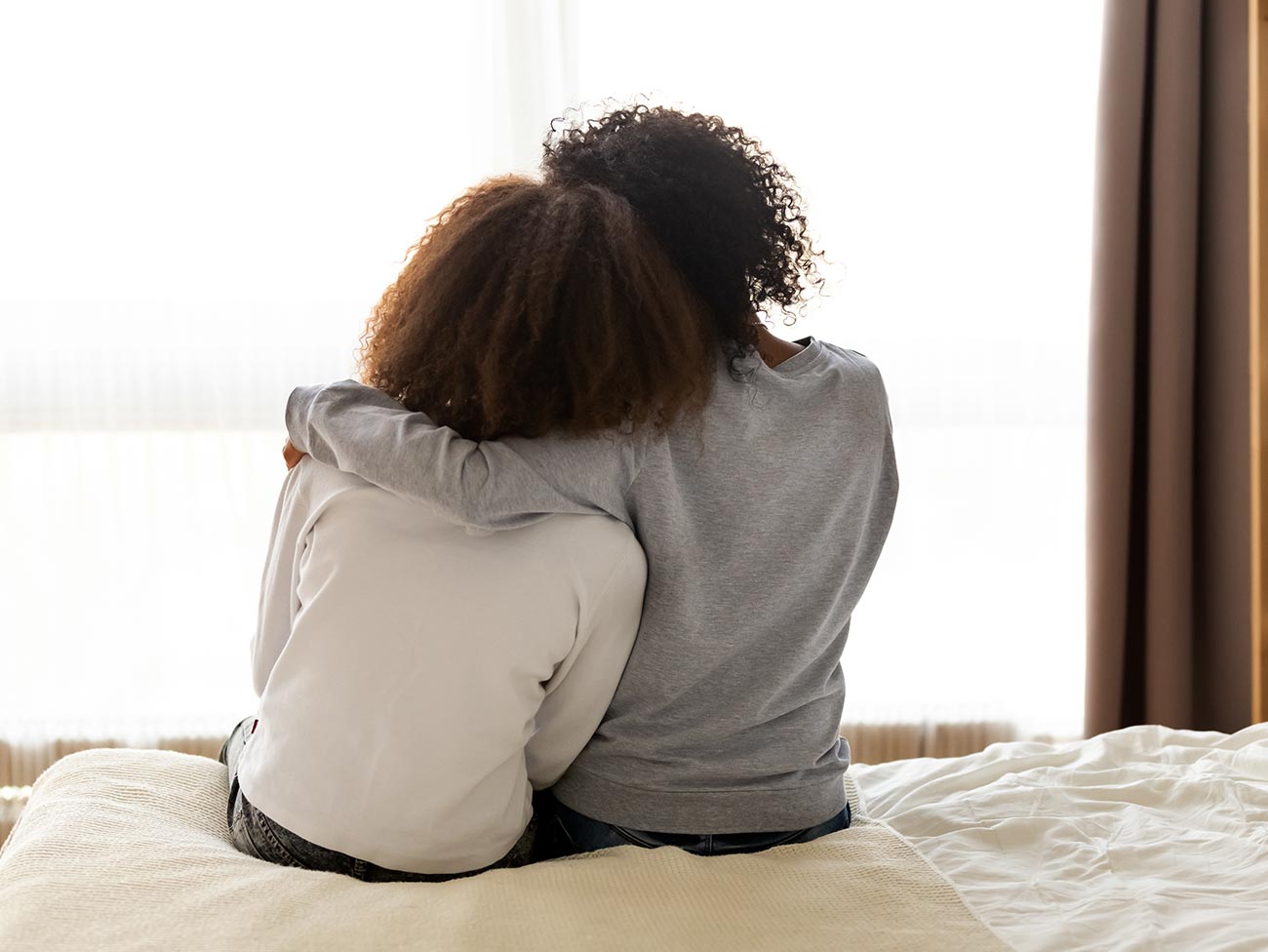 2 young people sitting on a bed with their arms around each other's shoulders