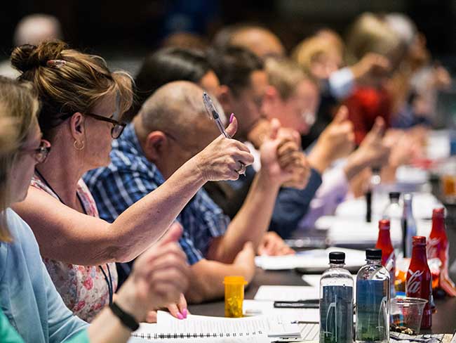 A group of people seated at a conferenced table voting during a bargaining session by giving a thumbs up. 