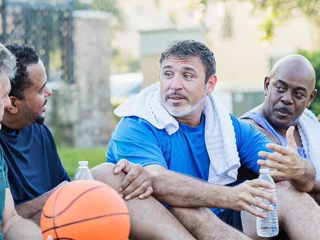 4 men on an outdoor basketball court sitting and talking