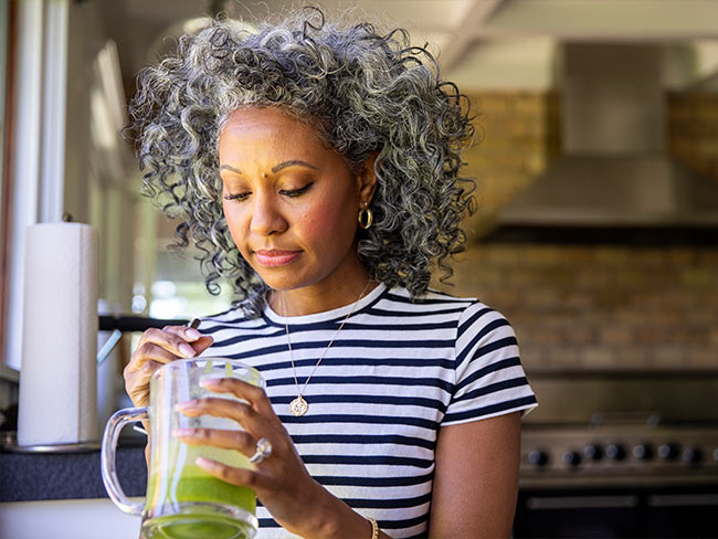 Black woman stirring a glass of green juice.