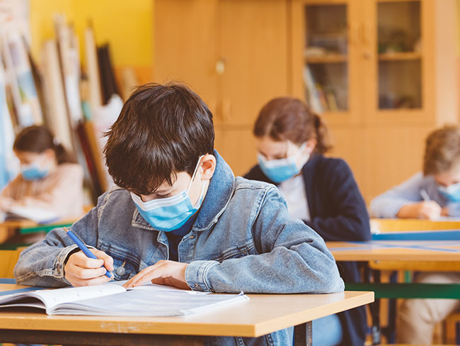 Boy wearing a face mask in a classroom with other kids