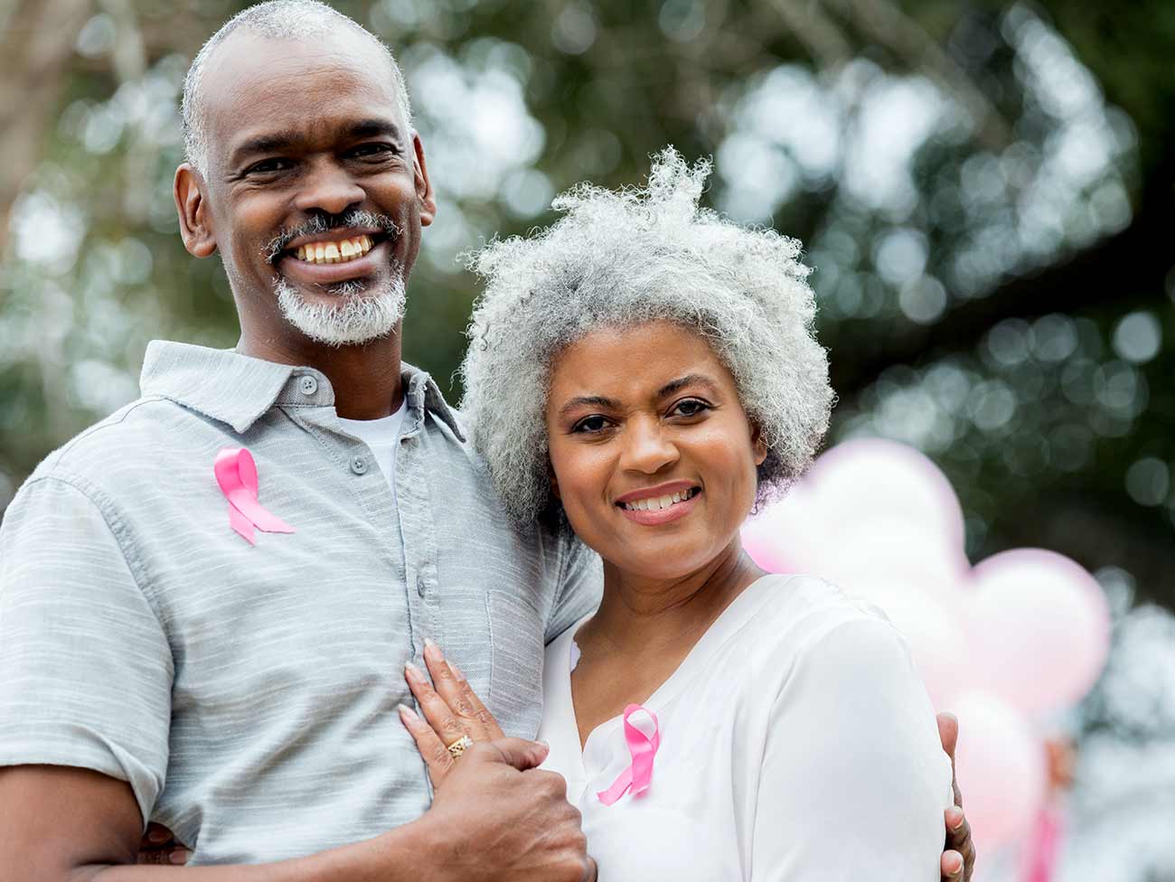 Smiling senior man and woman, both are wearing pink breast cancer awareness ribbons. 