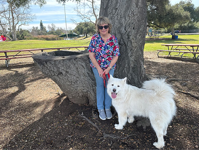 Woman standing outside by a tree with her white dog.