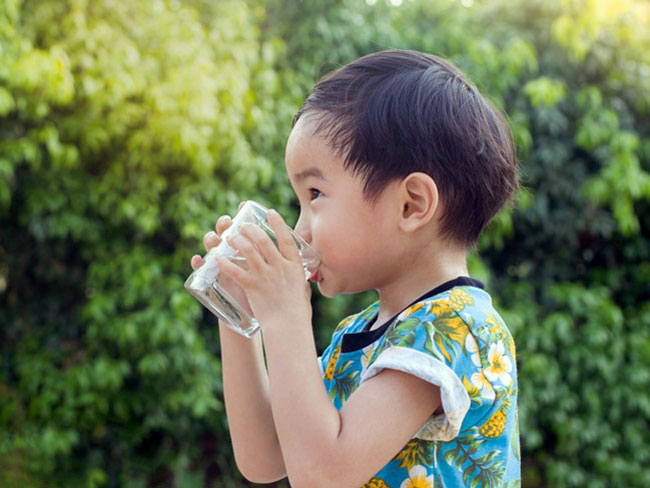 young boy in an outdoor setting drinking a glass of water