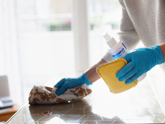 hands wearing rubber gloves cleaning a surface using a spray bottle and rag