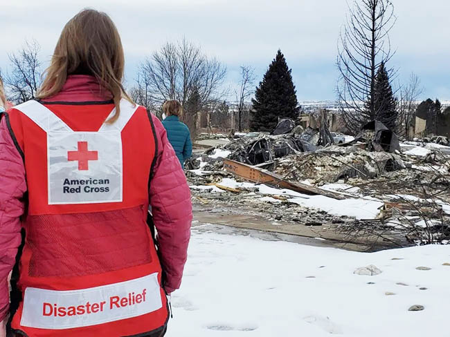 A Red Cross volunteer standing in front of a burned area.