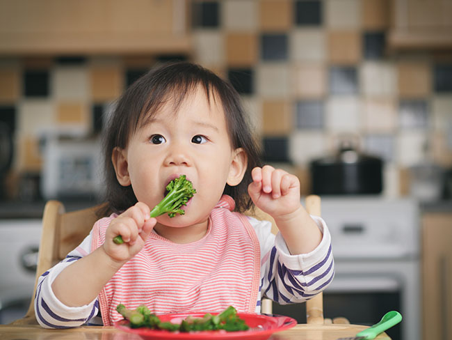 Baby girl eating vegetables while sitting on high chair at home