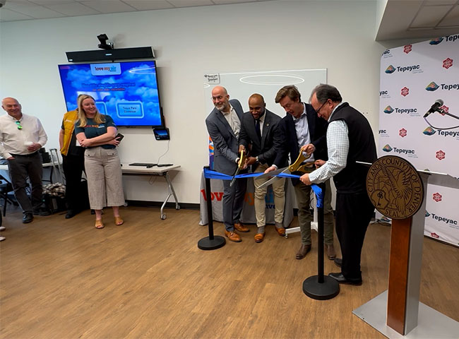  men doing a ribbon cutting ceremony with bystanders watching