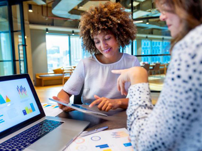 Women reviewing charts on a tablet and laptop.