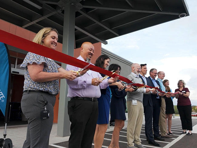 A group of people standing behind a long ribbon, cutting it during a ribbon cutting ceremony to celebrate the opening of a building.