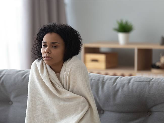sick woman sitting on a sofa wrapped in a blanket