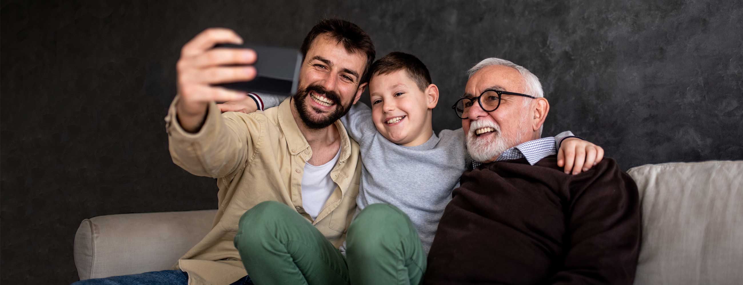 A grandfather, father and son smiling as they take a selfie together. 