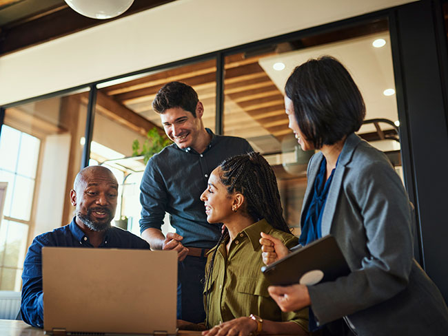 Happy coworkers in business attire gather around a laptop