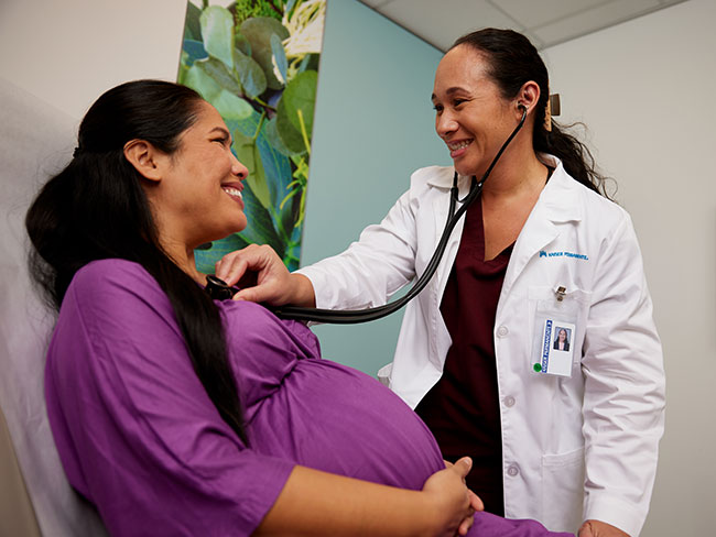 A doctor is examining a smiling pregnant woman