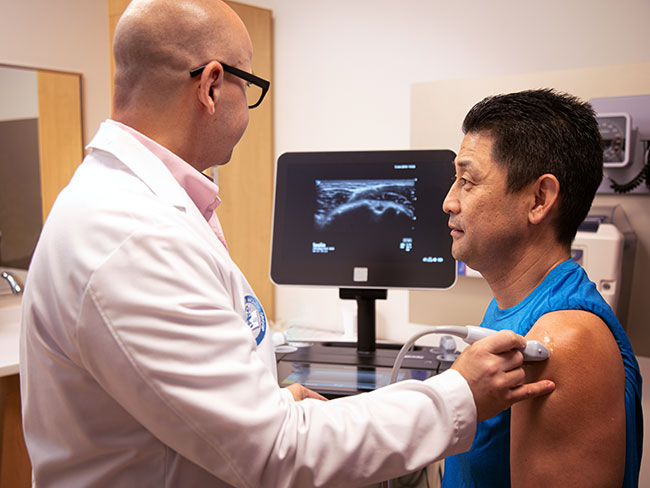 A doctor is using an ultrasound wand on a mans shoulder and looking at the display