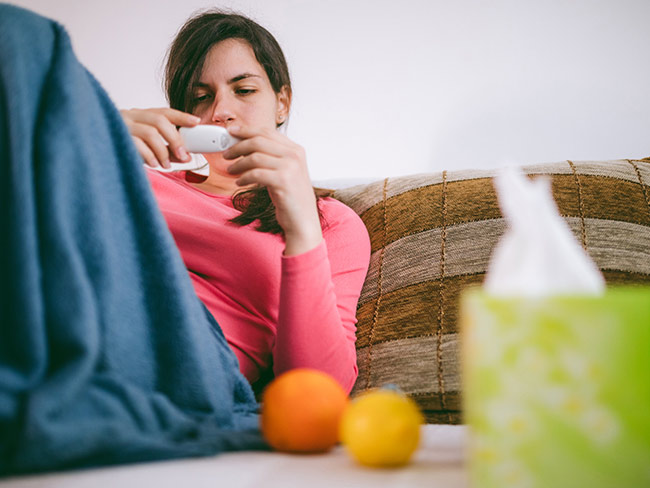 Woman with cold or flu on couch, checking temperature