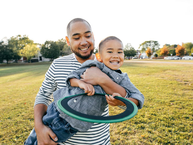 smiling young boy holding frisbee while being carried in his dad's arms