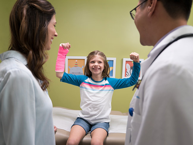 Girl with a pink cast on her arm in a power pose.