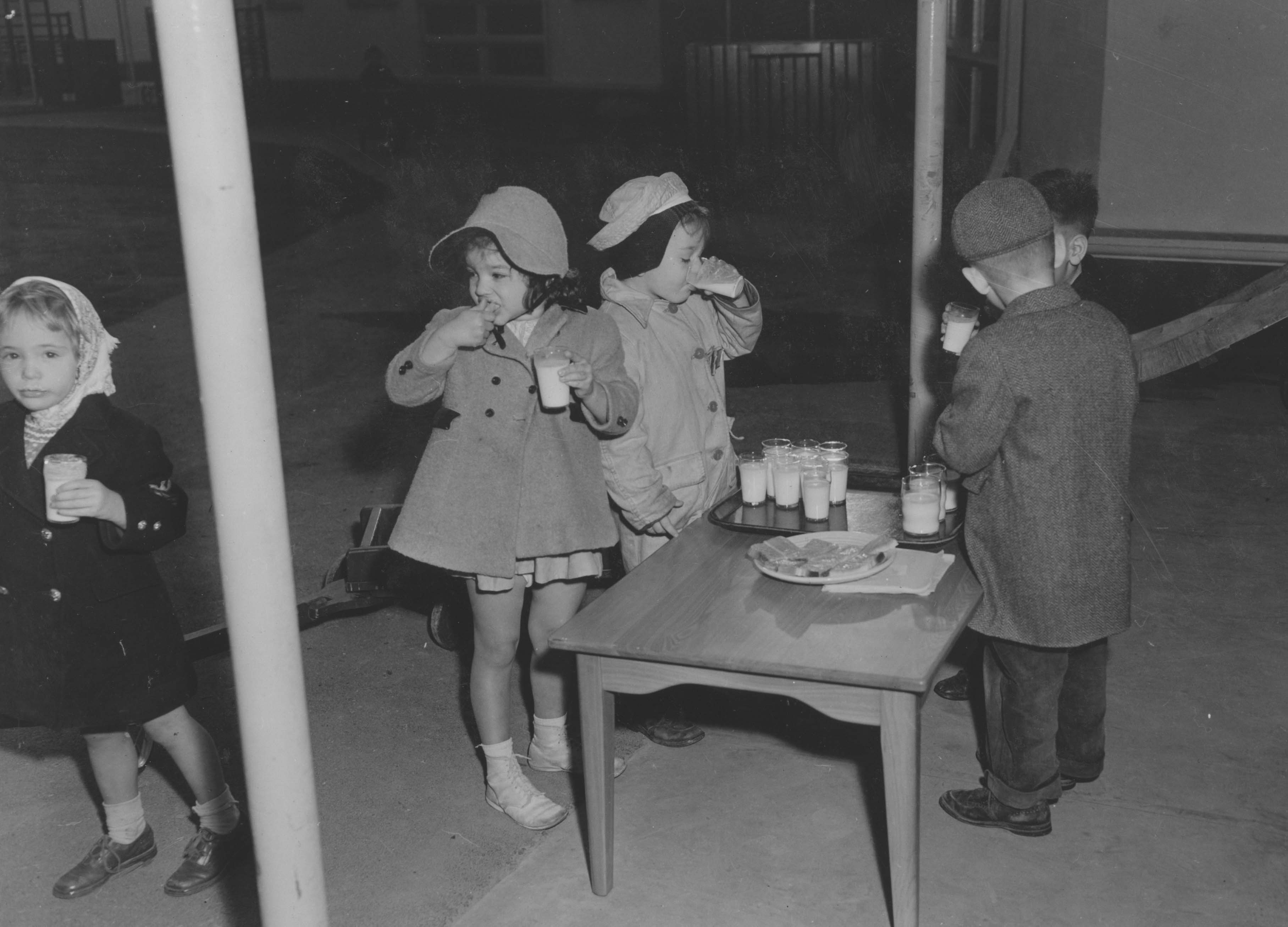 Black and white image from the 1940's of young boys and girls having a snack.