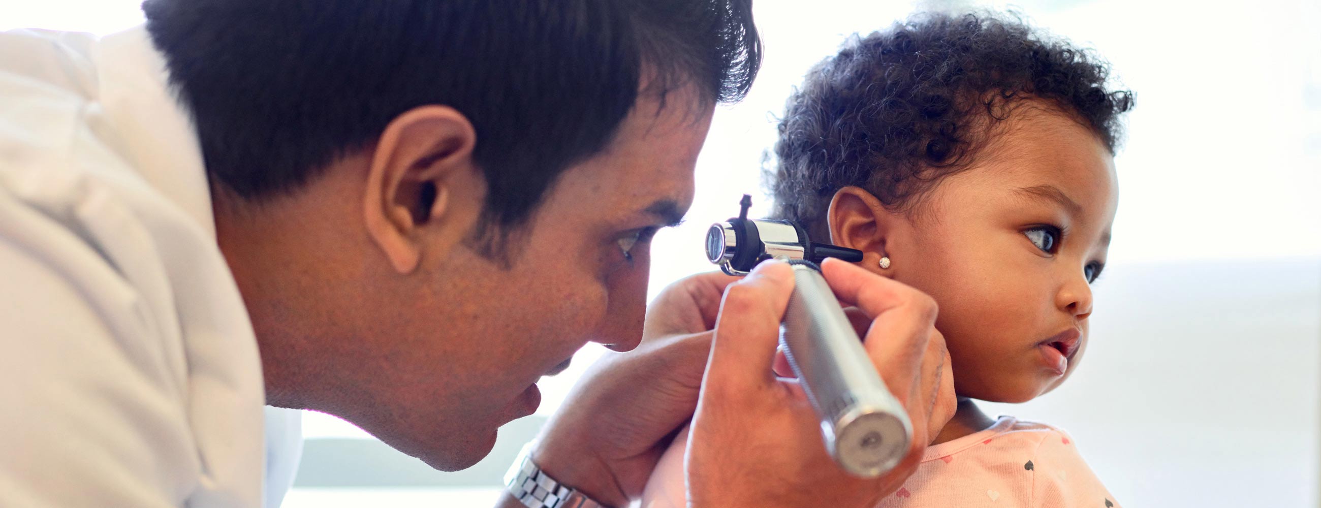 A male physician looking in the ear of a young toddler girl.