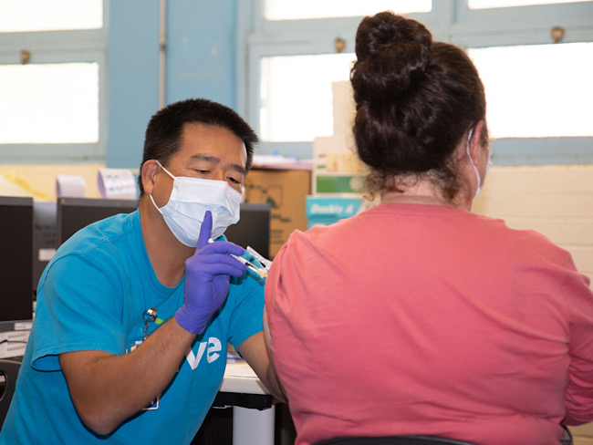 Sean Masaki, RN, vaccinates a parent at Aina Haina Elementary School on Oahu. 