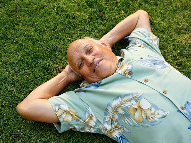 Man laying in the grass with arms behind his head.
