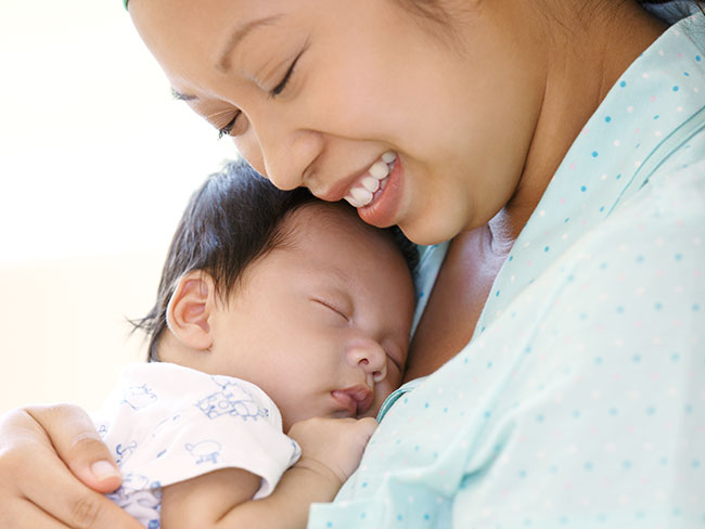 A smiling mother holding her newborn baby.