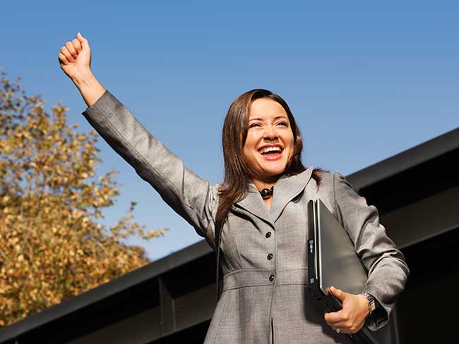 A young woman in a business suit with a fist raised over her head. 